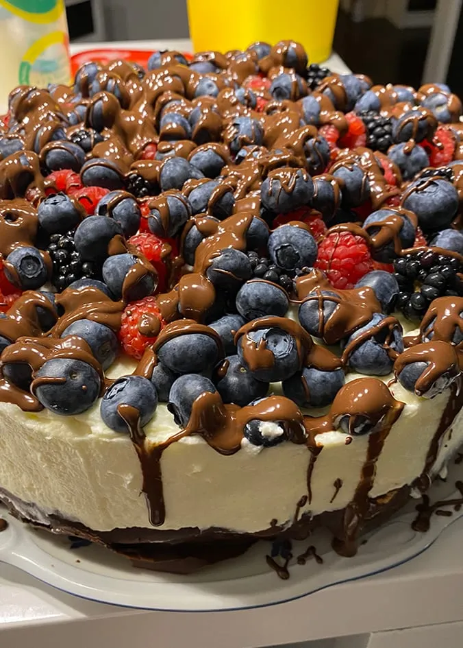 Cremetorte mit Blaubeeren, Himbeeren, Brombeeren und Schokoladenglasur auf einer Tortenplatte