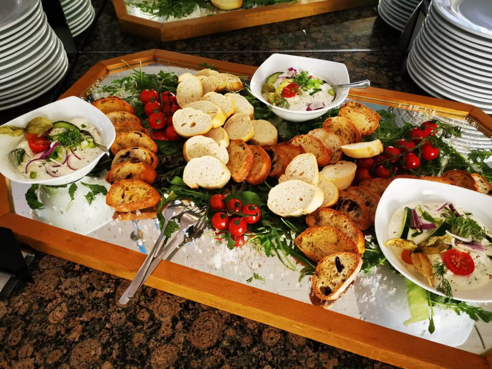 Brotplatte mit Baguette- und Ciabattascheiben auf Rucola, dazu Dips in weißen Schalen