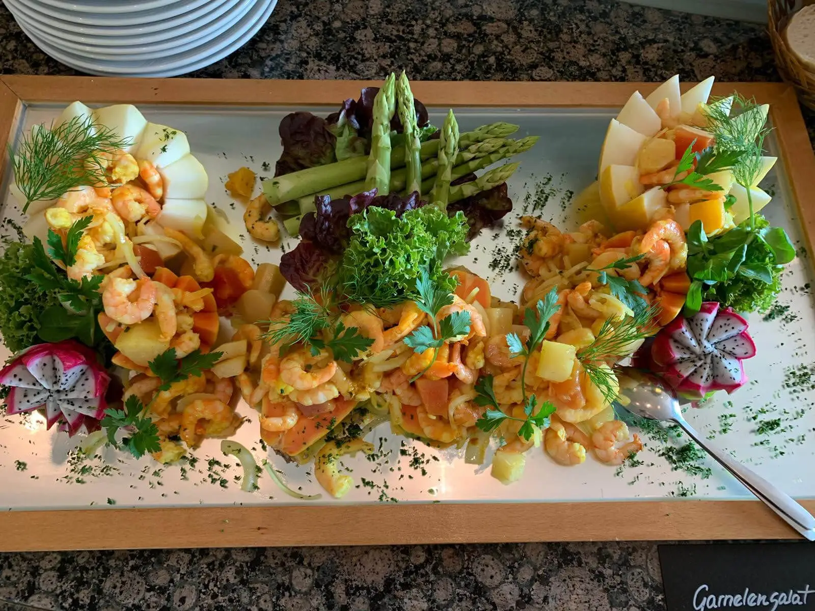Garnelensalat in Melonenschiffchen angerichtet, dazwischen grüner Spargel und Dill auf Spiegelplatte
