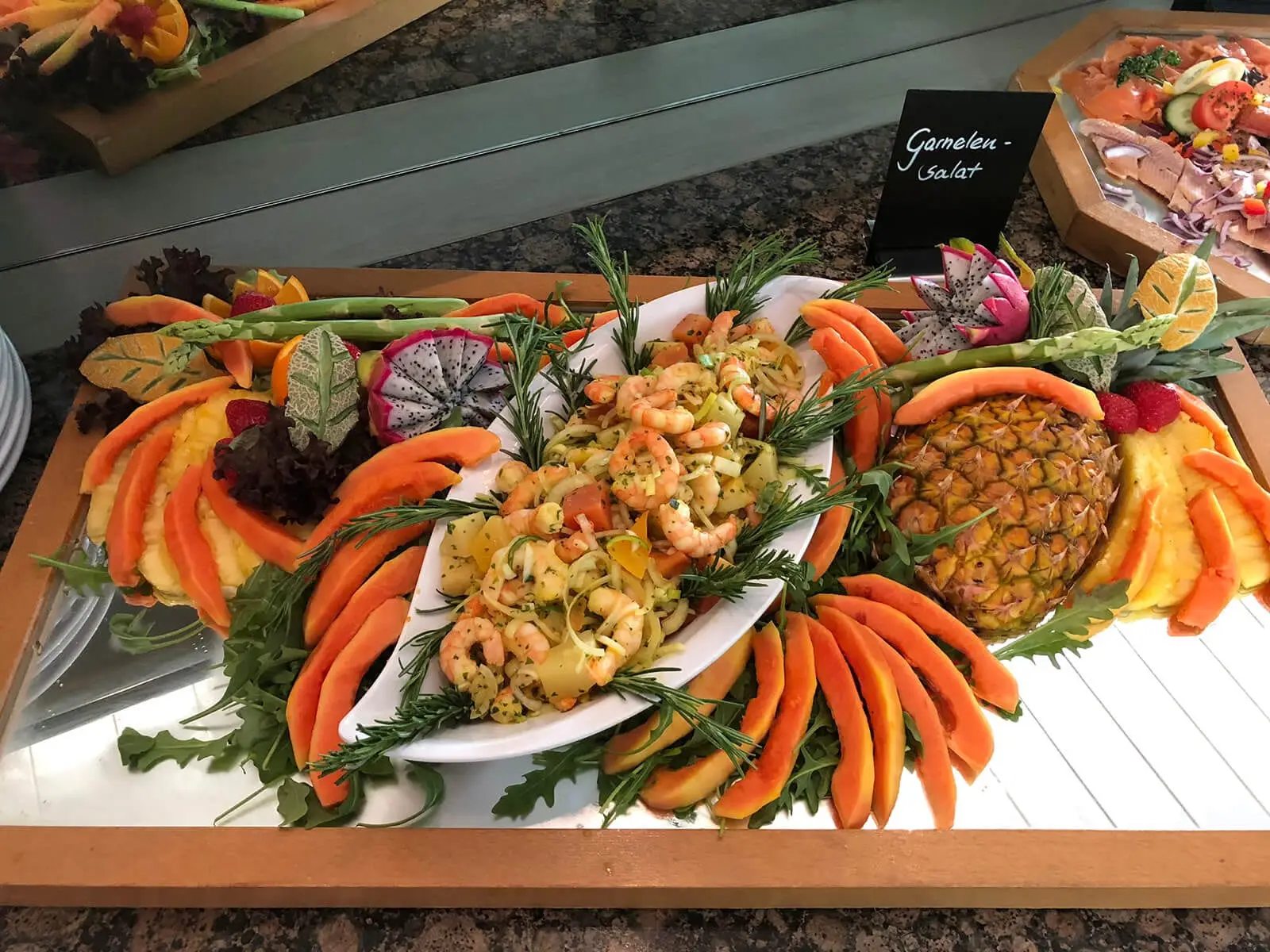 Buffetplatte mit Garnelensalat und Papaya, dahinter Schild mit Aufschrift Garnelen-Salat