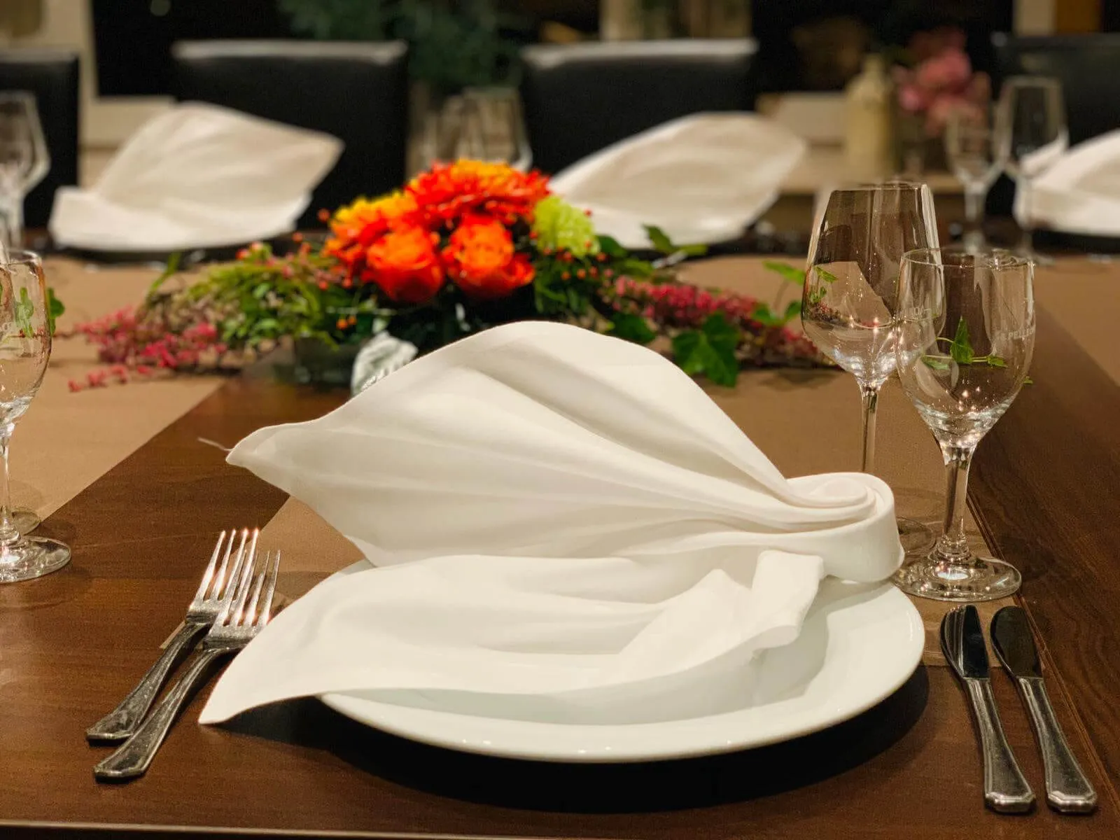 Gedeck mit kunstvoll gefalteter weißer Serviette und herbstlichem Blumengesteck