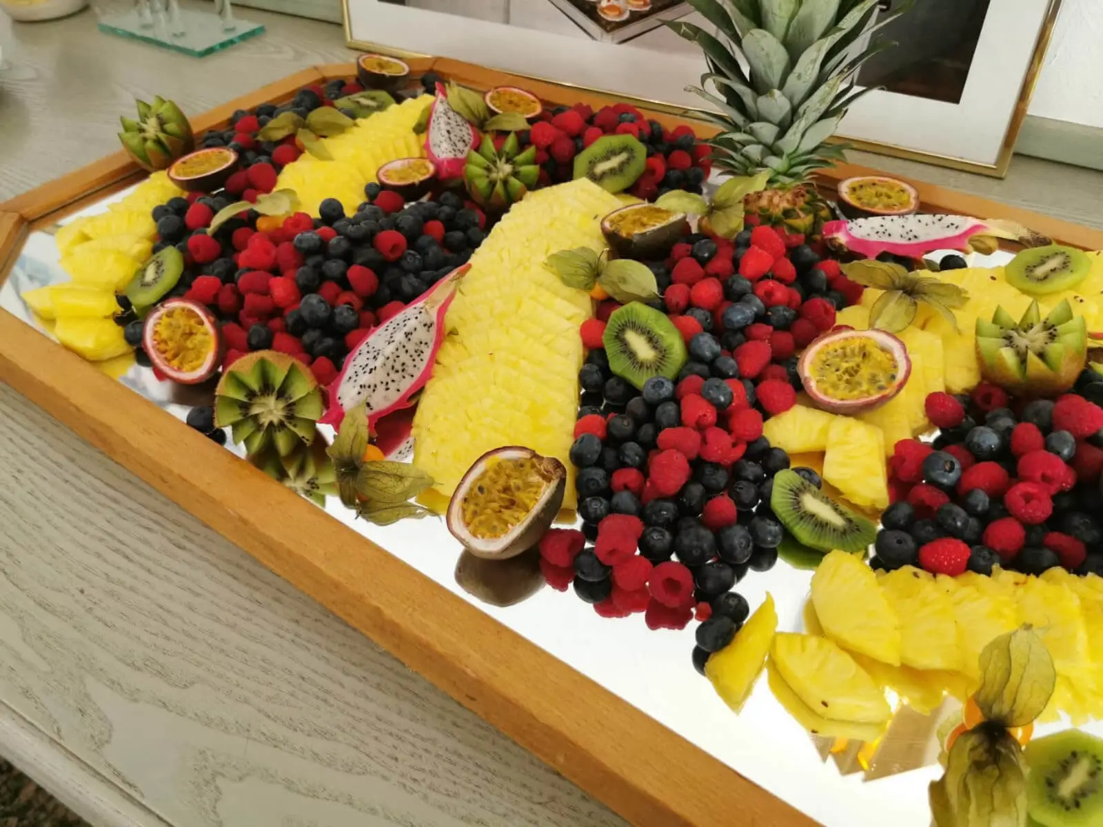 Spiegelplatte mit aufgefächerter Ananas, Beeren und Kiwi, dekoriert mit Physalis