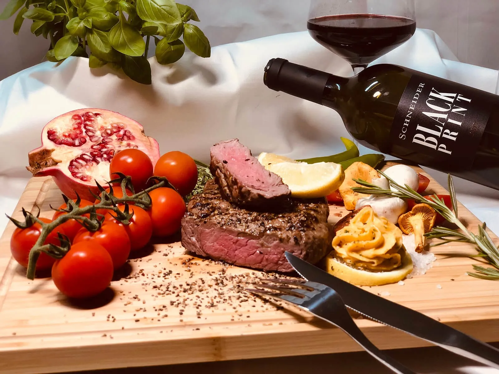 Angeschnittenes Rinderfilet auf Holzbrett mit Kräuterbutter, Tomaten, Pilzen und Rotwein