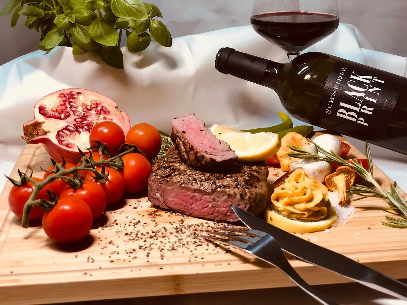 Angeschnittenes Rinderfilet auf Holzbrett mit Kräuterbutter, Tomaten, Pilzen und Rotwein