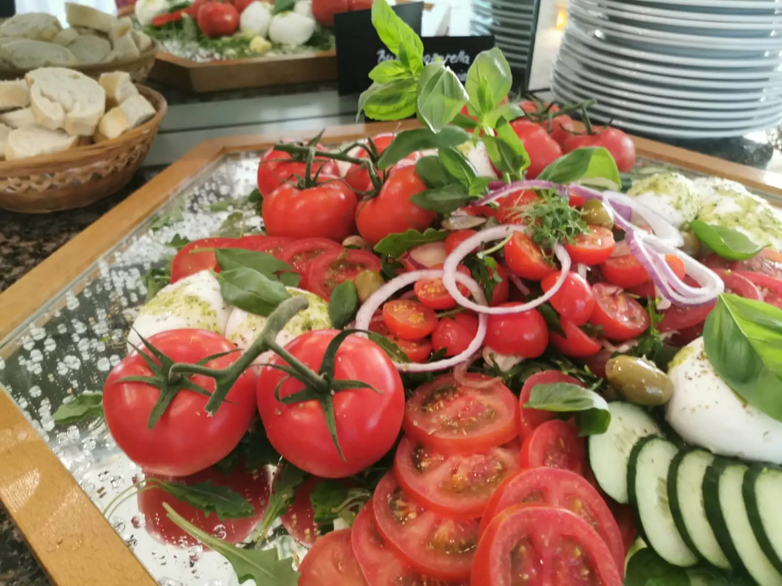 Nahaufnahme von Rispentomaten, Mozzarella und Basilikum, im Hintergrund Brotkorb mit Baguette