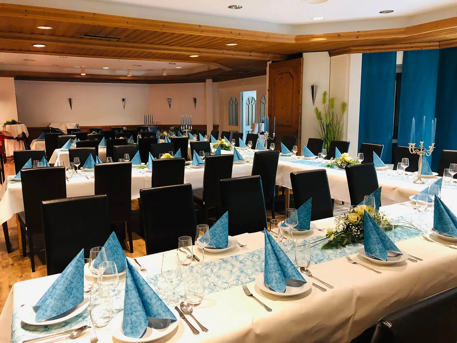 Festlich eingedeckte Tafeln im Saal mit blauen Servietten und Kerzenleuchtern