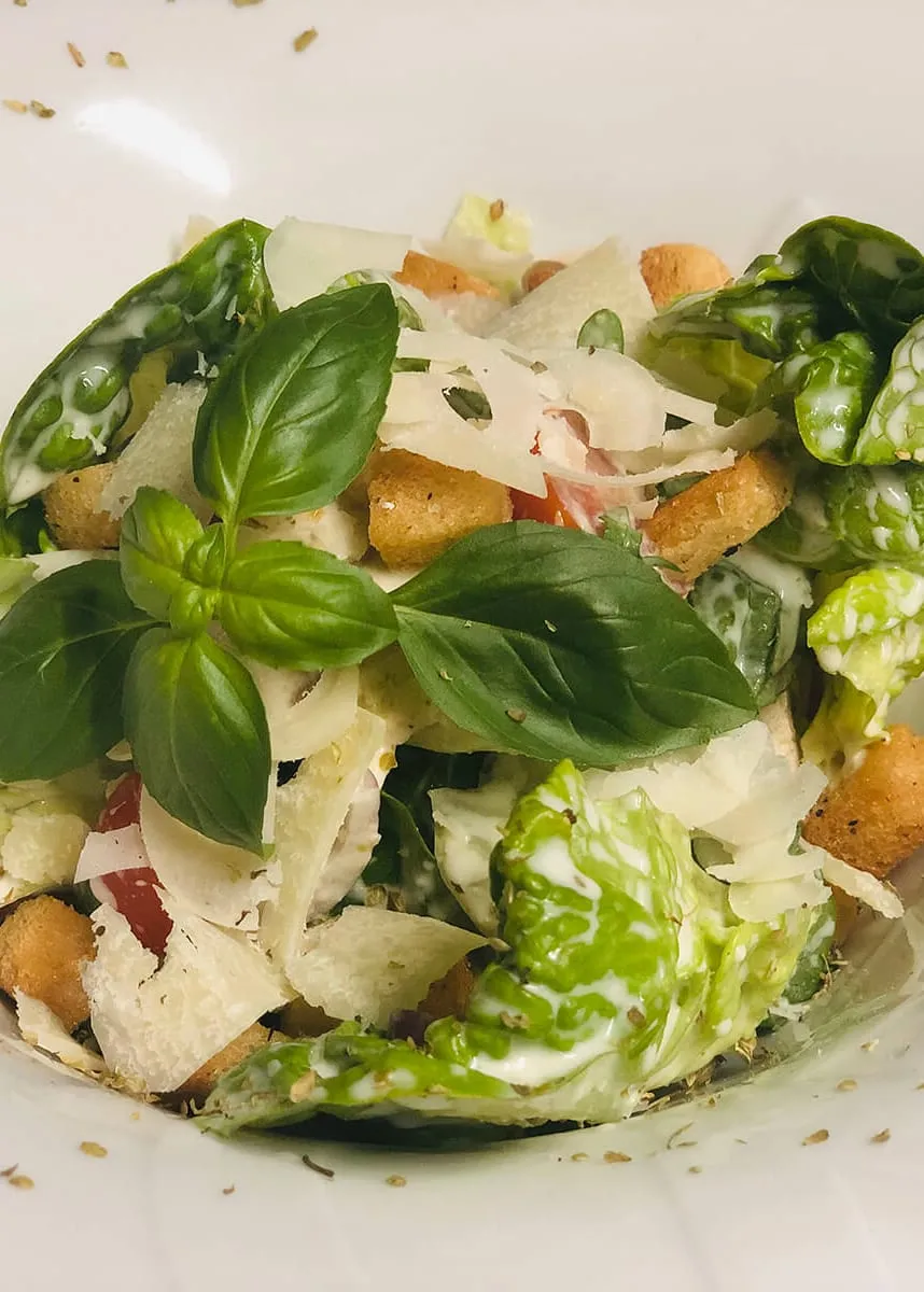 Salat mit Römersalat, Basilikum, gehobeltem Parmesan und Croûtons in einer weißen Schale