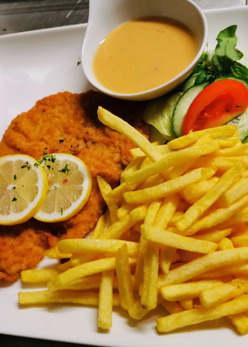 Paniertes Schnitzel mit Pommes frites, Zitronenscheiben, Salatgarnitur und heller Sauce