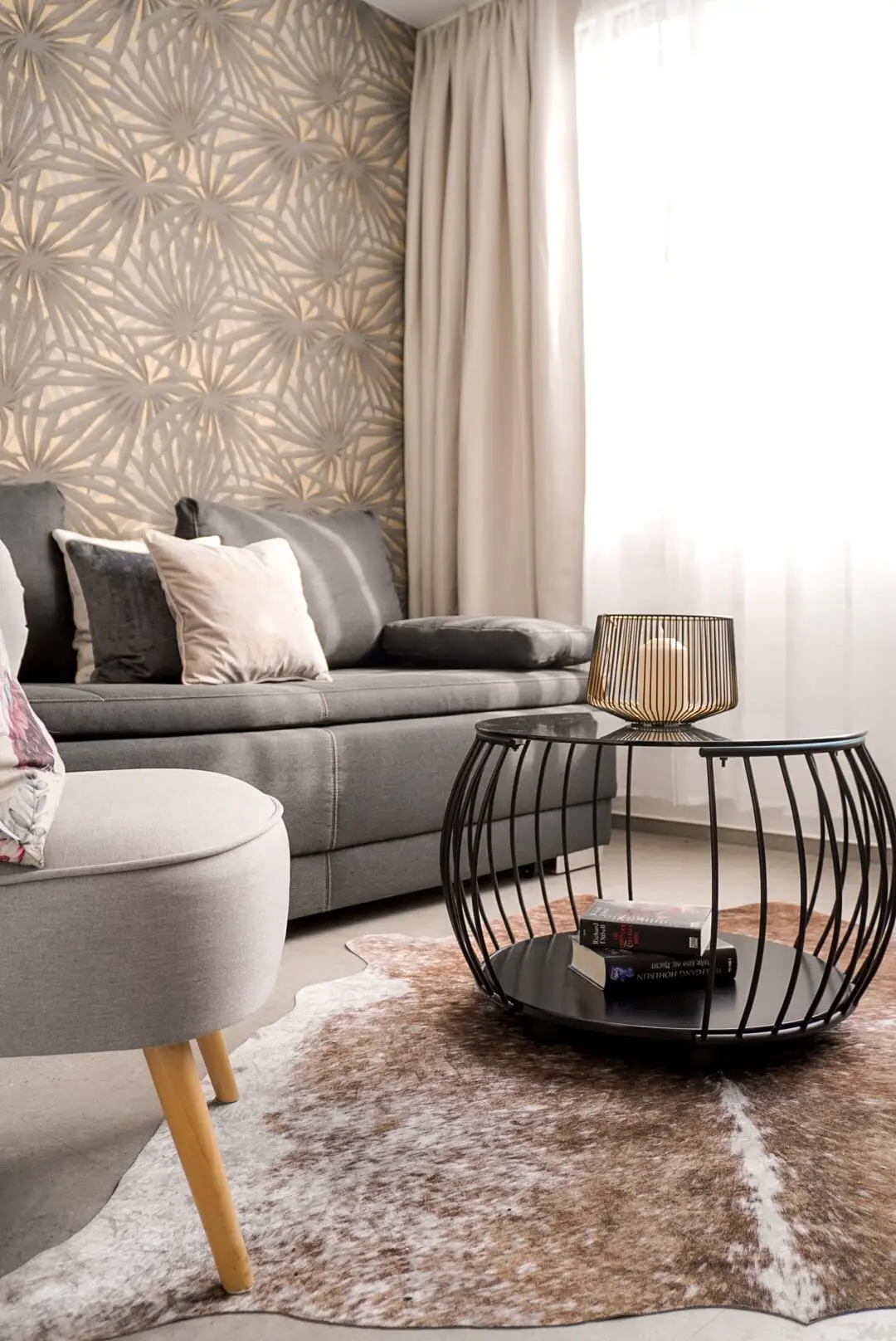 Sitzecke mit grauem Sofa, Kissen, rundem Drahtkorbtisch und Fellteppich am Fenster