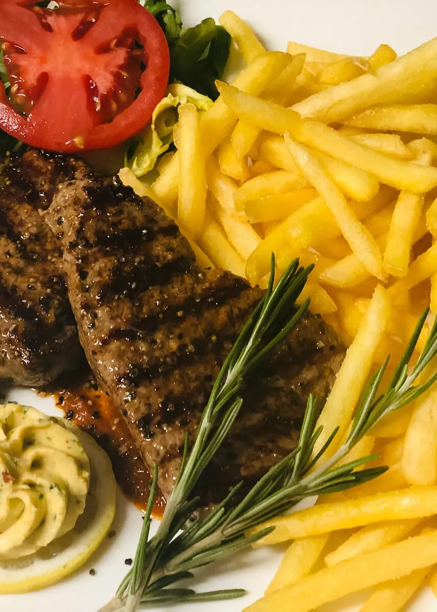 Gegrilltes Steak mit Pommes frites, Kräuterbutter, Tomatenscheibe und frischem Rosmarin