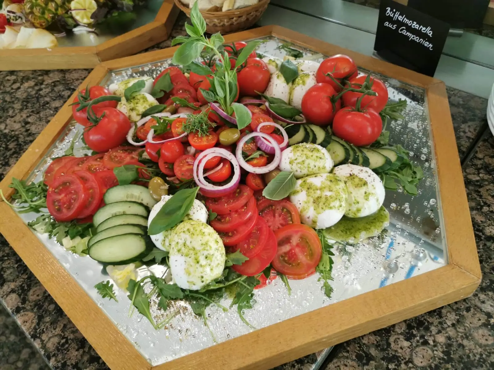 Tomaten mit Büffelmozzarella und Rucola auf Spiegelplatte, dahinter Schild aus Campanien
