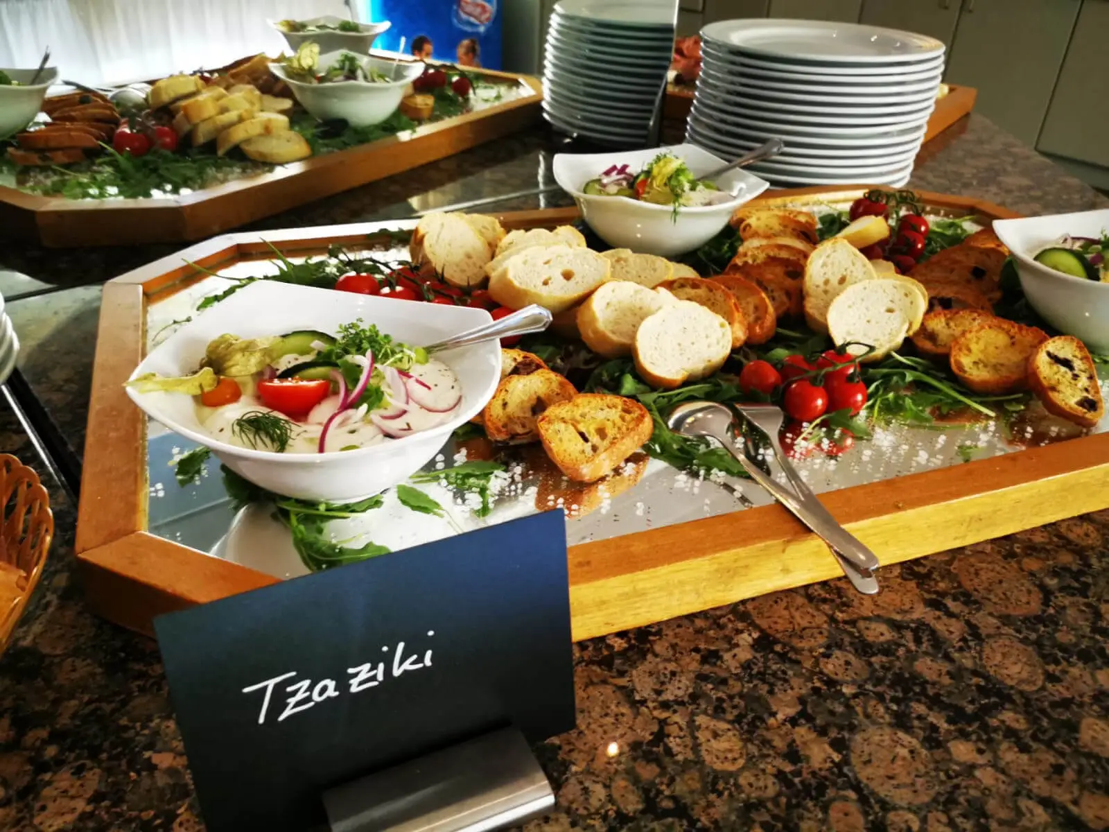 Tafelschild mit Aufschrift Tzaziki vor Brotplatte mit Baguettescheiben und Kirschtomaten