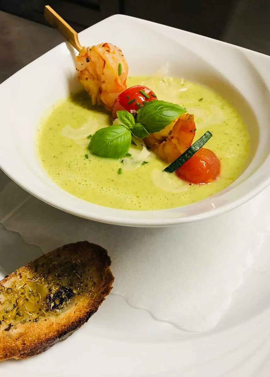 Grüne Zucchinicremesuppe mit Garnelenspieß, Kirschtomaten und Basilikum, dazu geröstetes Weißbrot